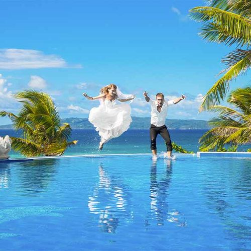 Couple de jeunes mariés se jetant dans une piscine habillés