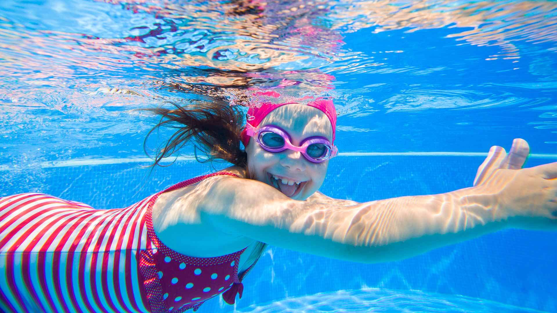 Petite fille avec lunettes de natation nageant sous l'eau tout sourire