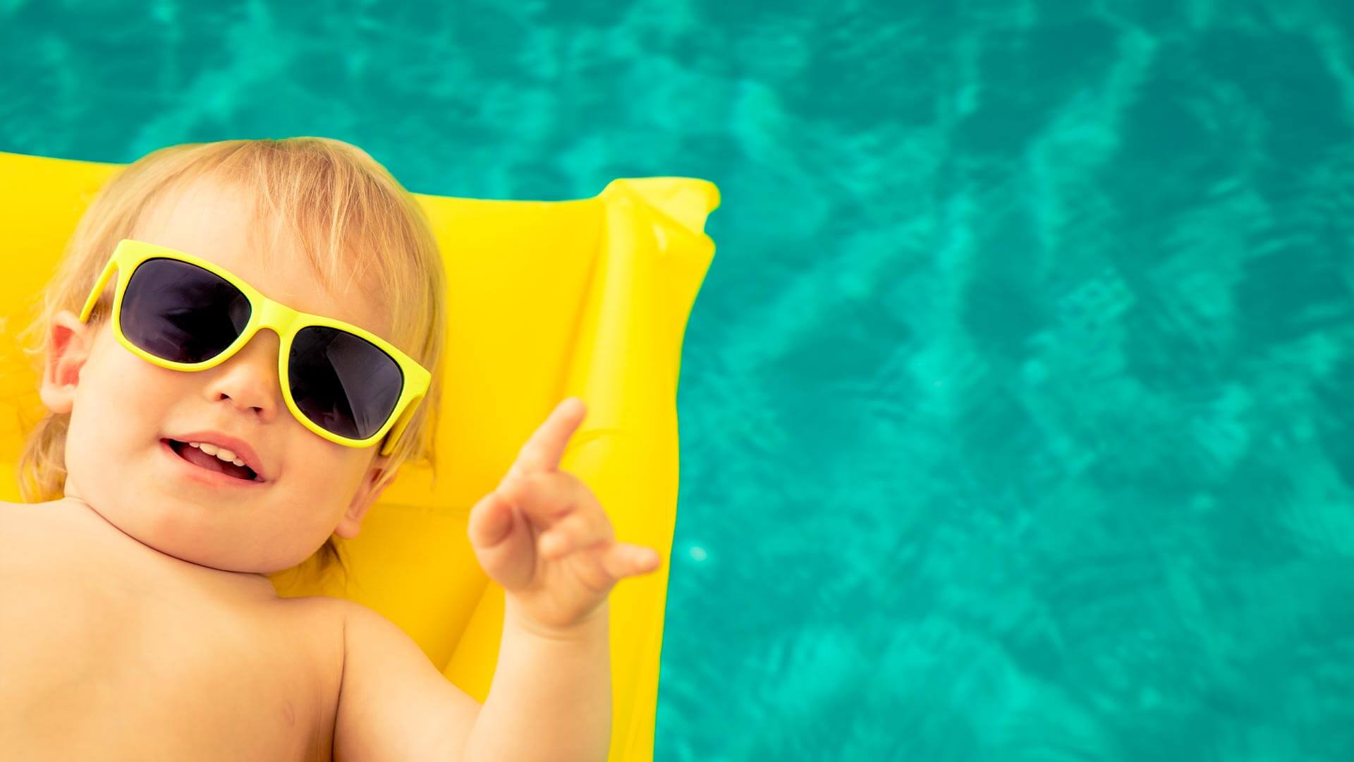 Enfant sur bouée gonflable avec des lunettes de soleil faisant le signe Rock N' Roll de la main