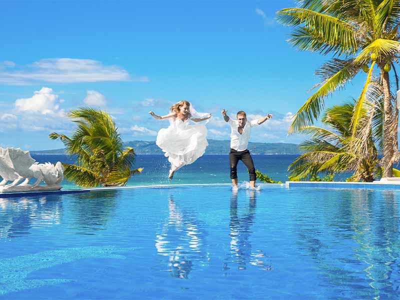 Couple de jeunes mariés se jetant dans une piscine habillés